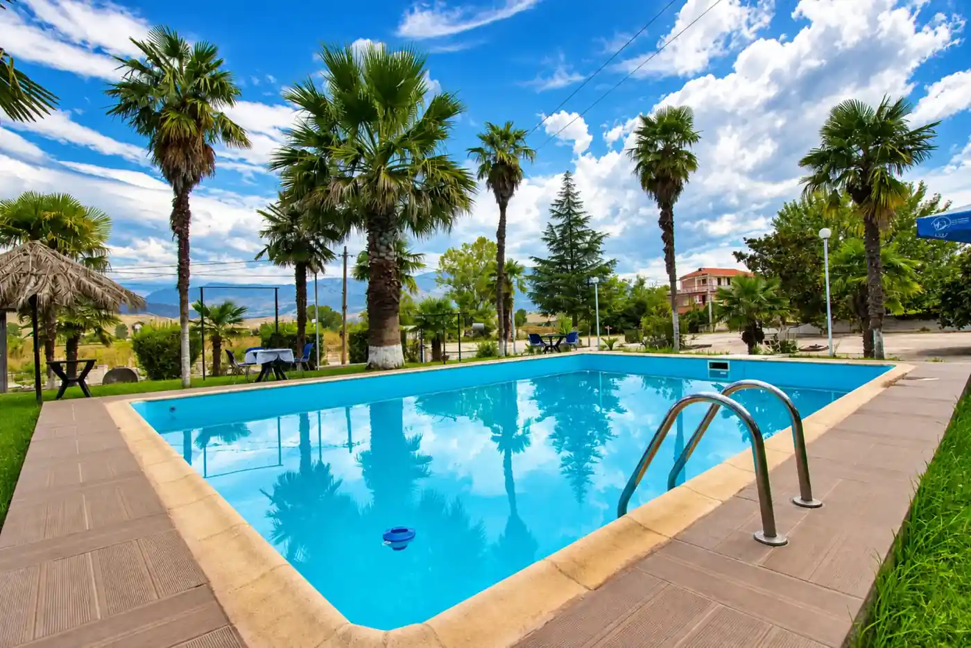 Pishina në ambient të hapur, e rrethuar nga palma nën qiellin blu
